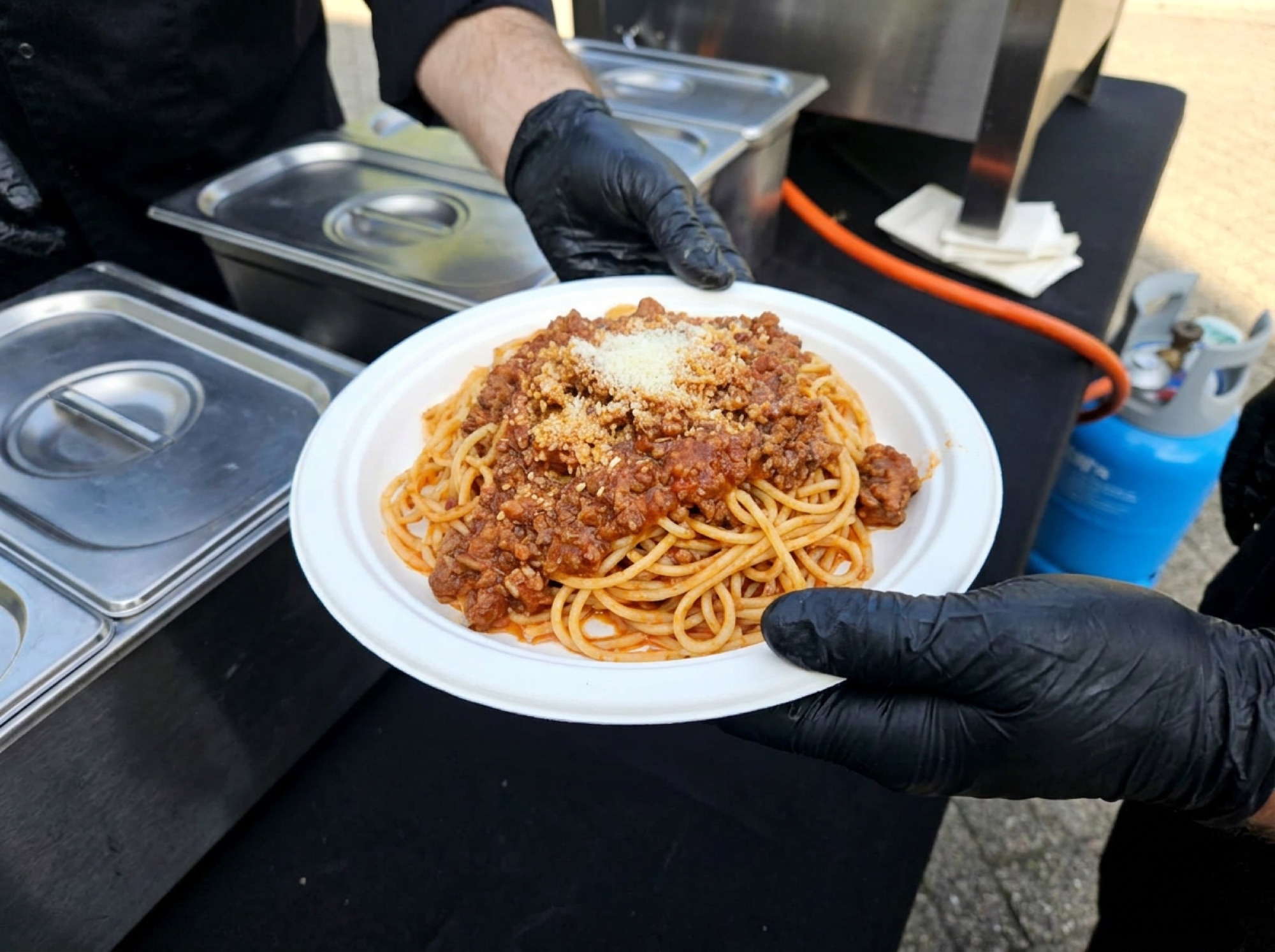 Pasta bolognese op wit suikerrietbord aan de cateringcounter, geserveerd met zwarte handschoenen