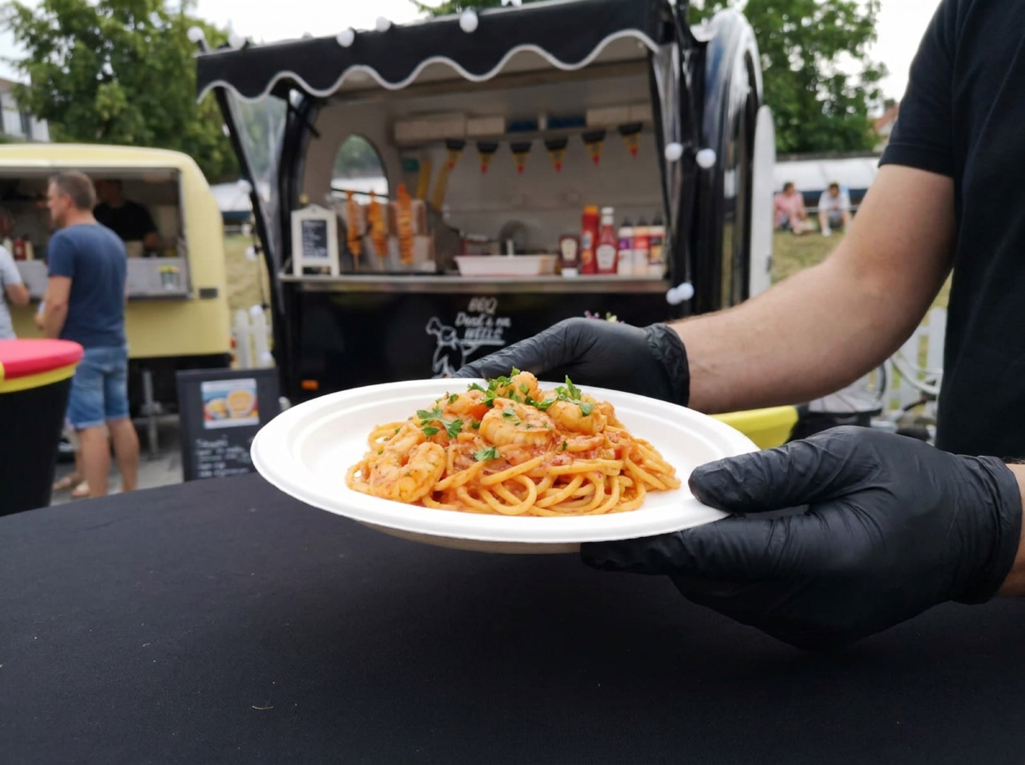 Pasta scampi diabolique op wit suikerrietbord, vastgehouden met zwarte handschoenen aan de BBQ Deals trailer